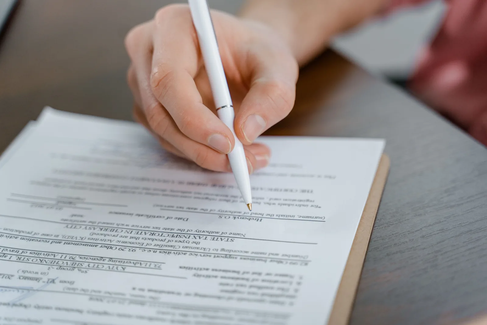 A hand holding a pen signing a document, close-up shot with focus on the paper. Creator rights operations guide: accounts, team roles, asset libraries, releases, metadata, approvals