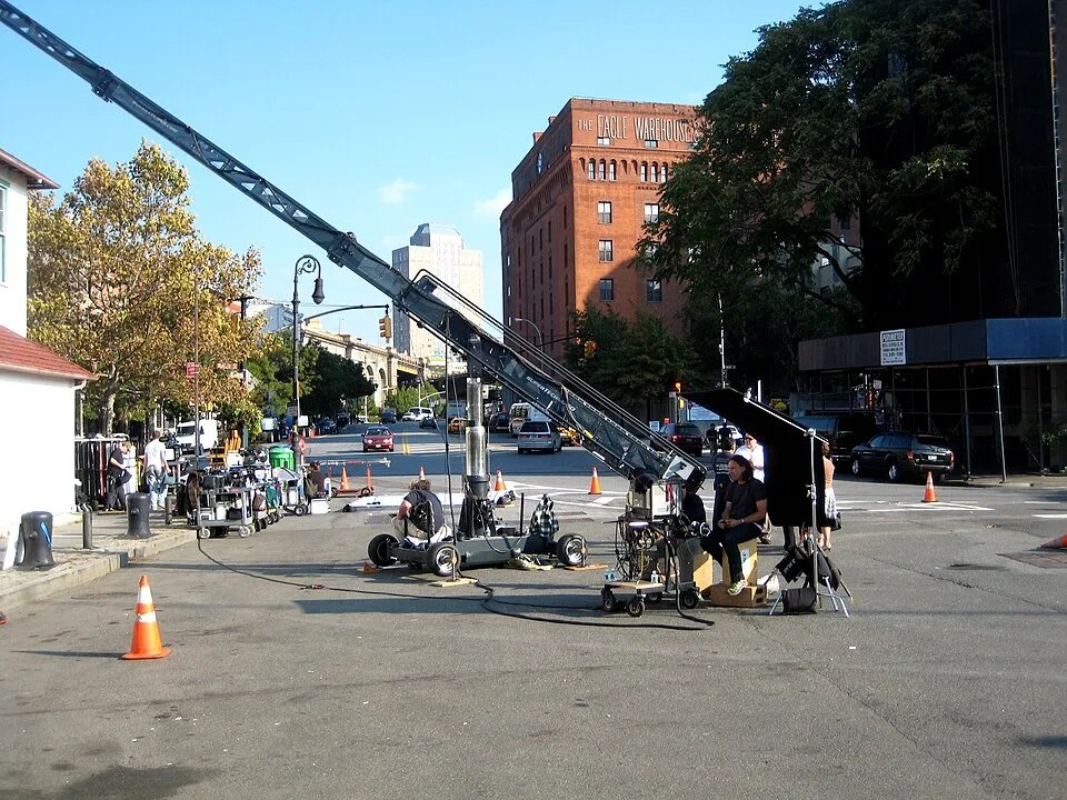Production equipment, a long camera crane, carts, cables, cones, and several people occupy part of a city street.