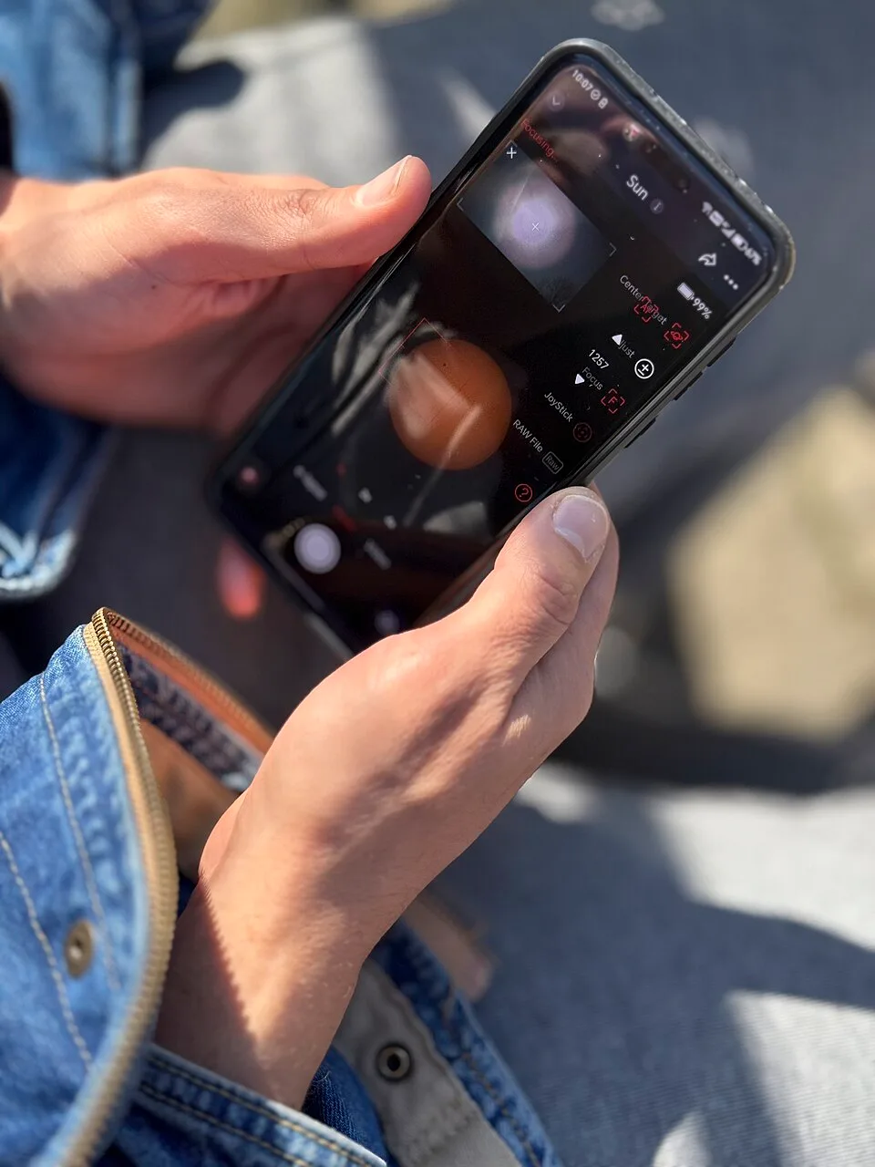 Hands hold a smartphone displaying a camera interface in bright outdoor light.
