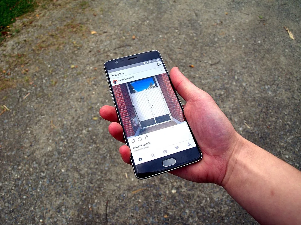 A hand holds a smartphone displaying a social-media post with a photograph of a door.