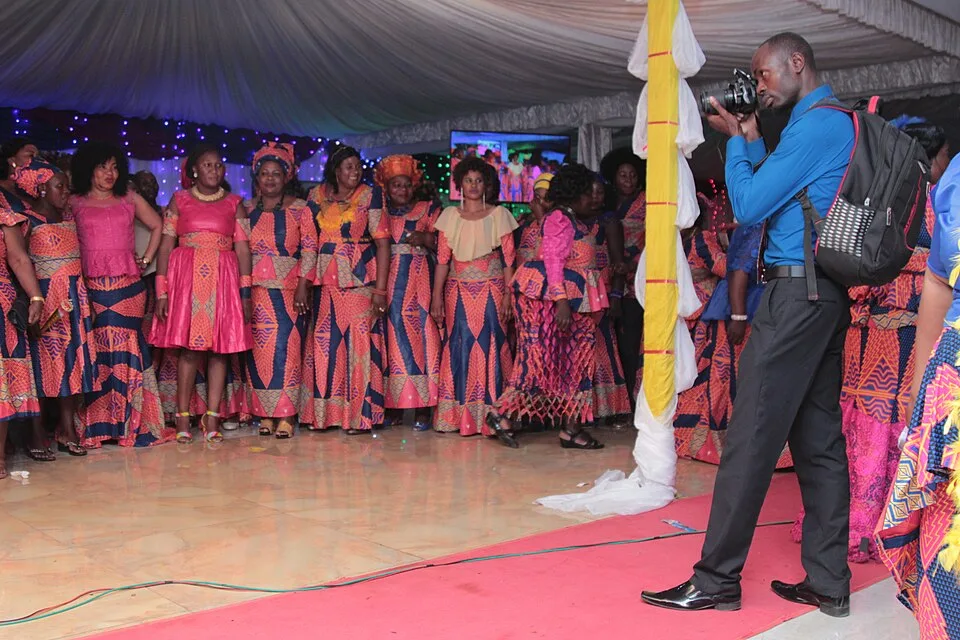 A photographer holds a camera toward a group of people in matching patterned clothing inside a decorated event space.